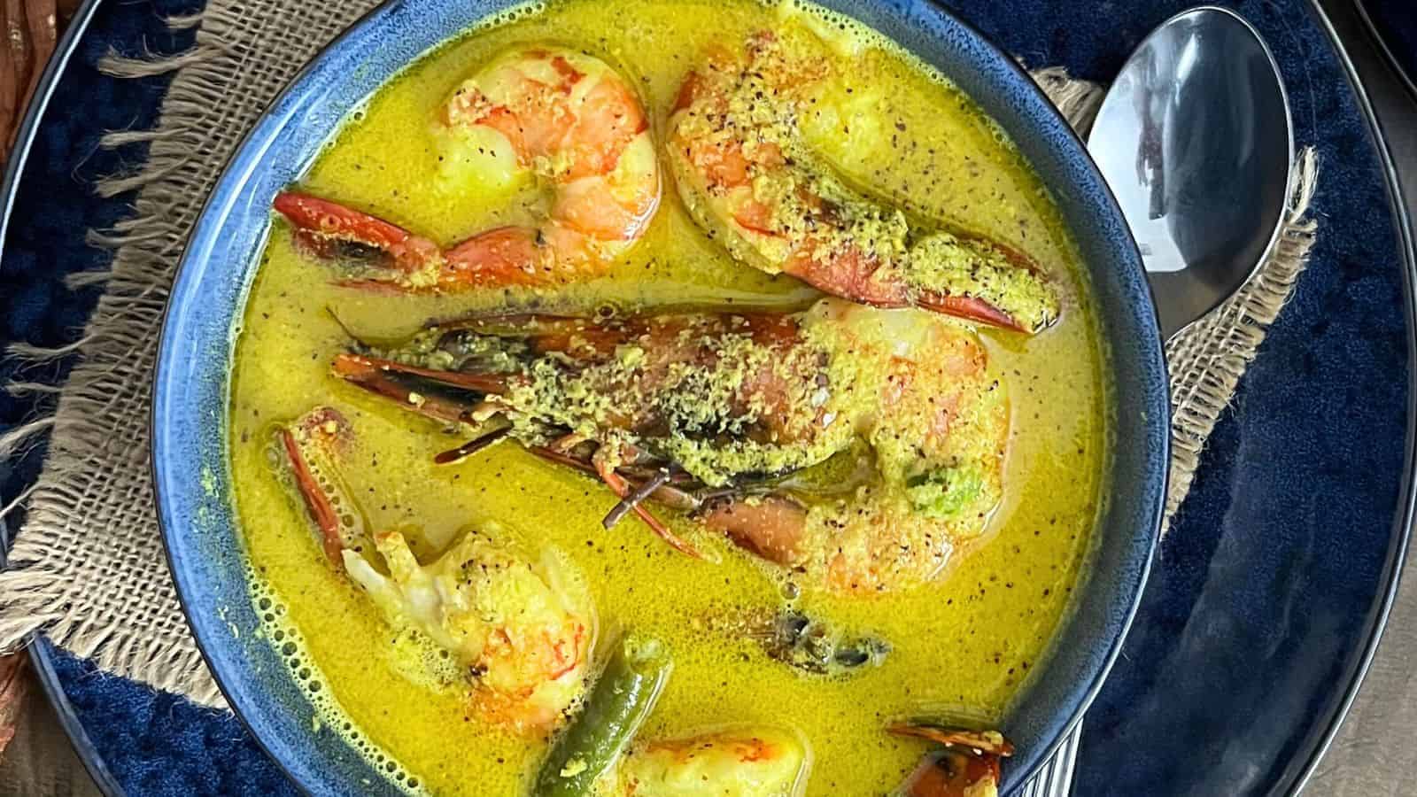 A bowl of Shrimp Coconut Curry Instant Pot, served on a blue woven placemat with a spoon on the side.