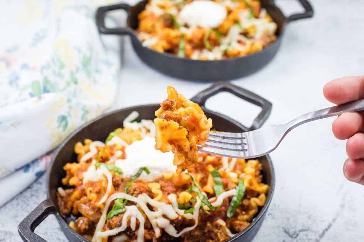 Two cast-iron skillets filled with skillet lasagna, topped with melted cheese.