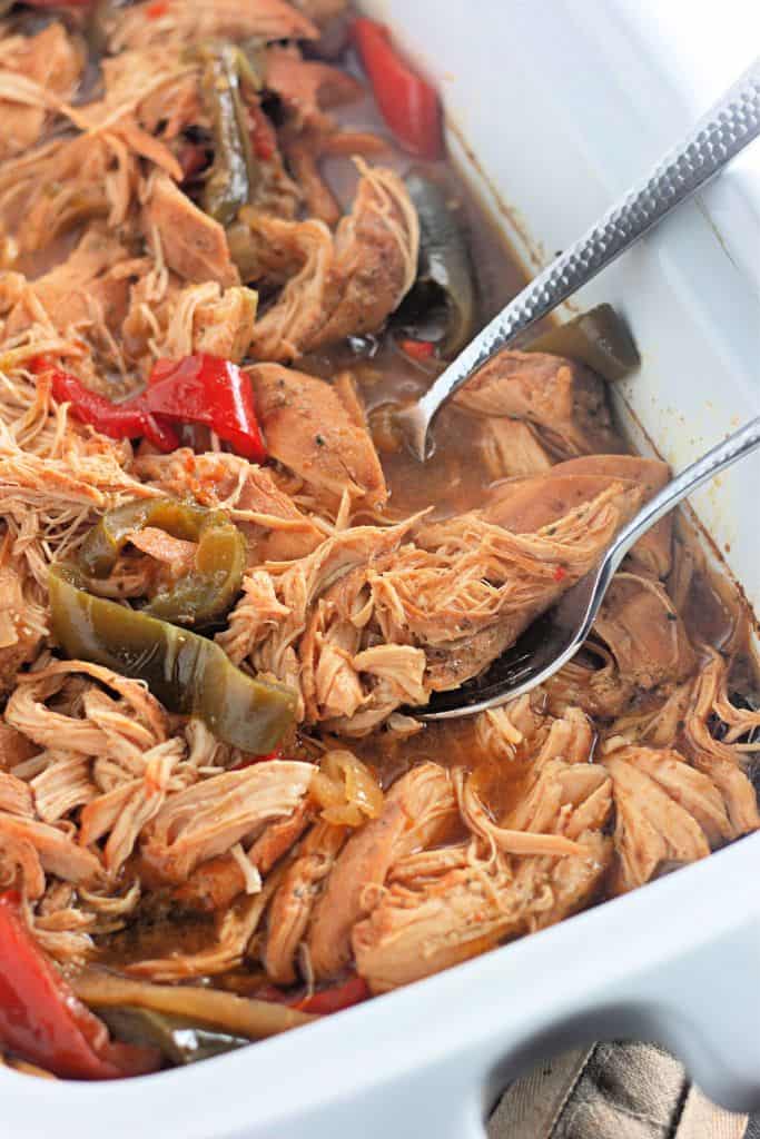 A shredded chicken cooked in a slow cooker with red and green bell peppers, and a flavorful broth.