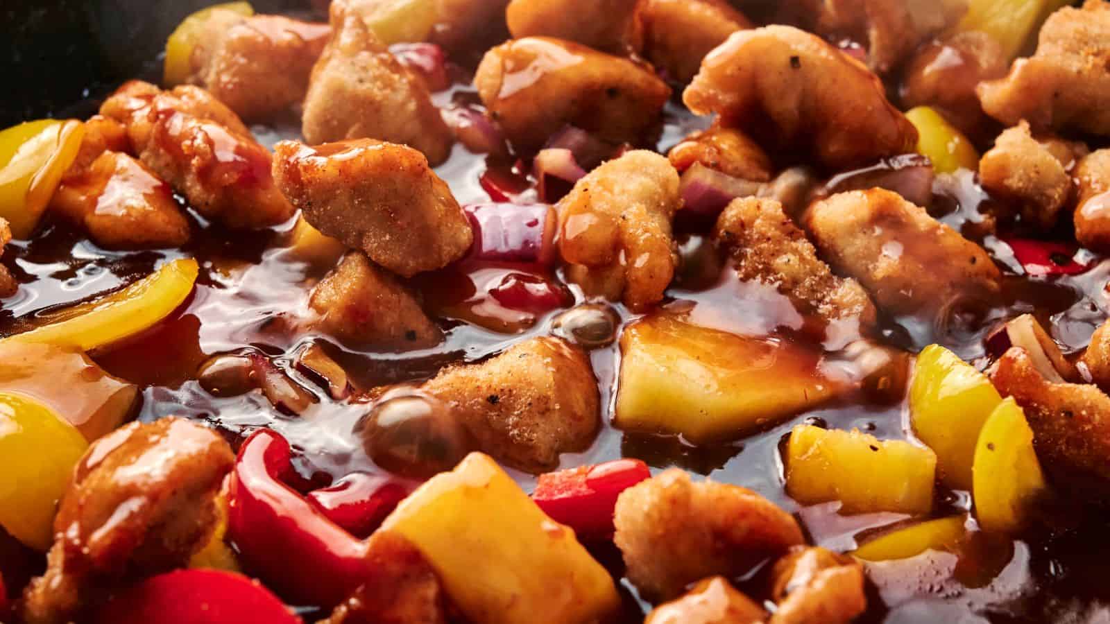 Close-up of sweet and sour chicken with bell peppers and pineapple chunks in a thick sauce.