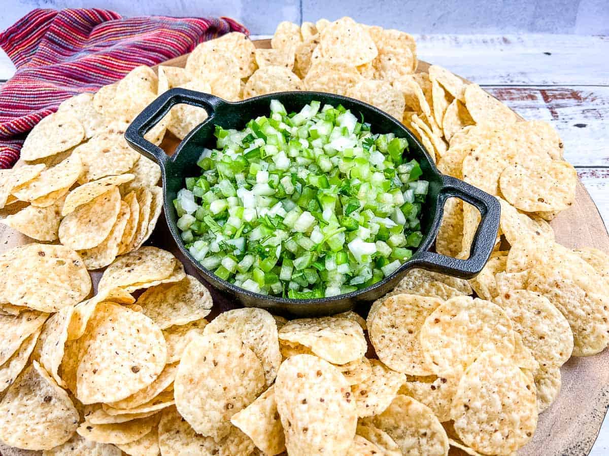 Tomatillo pico de gallo in a black dish surrounded by tortilla chips.