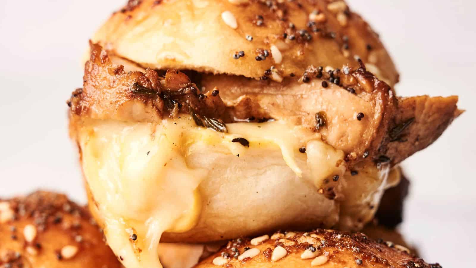 Close-up of a seasoned bagel sandwich with melted cheese and turkey slider filling, topped with seeds.