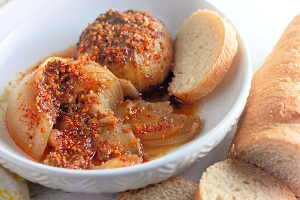 Two baked onions topped with a crunchy, flavorful coating, served with slices of white bread on the side.