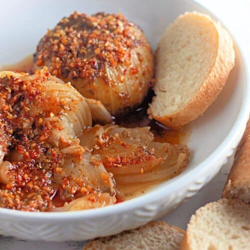 Two baked onions topped with a crunchy, flavorful coating, served with slices of white bread on the side.