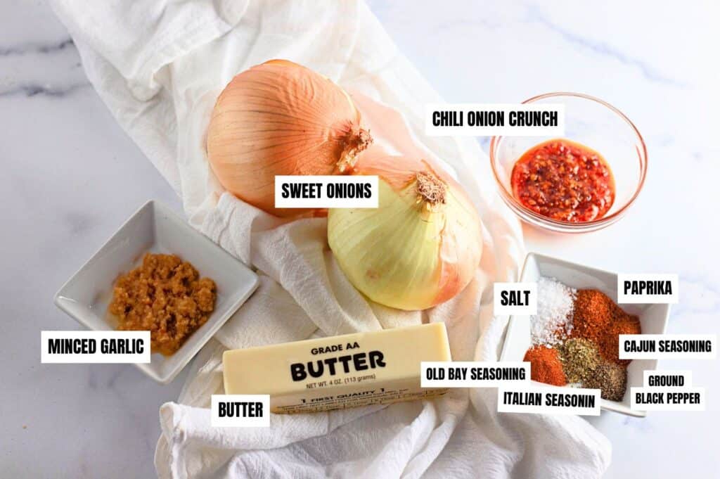 Ingredients for making a viral recipe onion boil: sweet onions, chili onion crunch, minced garlic, butter, salt, paprika, Cajun seasoning, Old Bay seasoning, Italian seasoning, and ground black pepper.