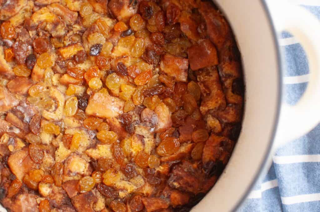 Close-up of a warm, golden-brown cinnamon roll casserole topped with plump golden and dark raisins, baked to perfection in a white dish.