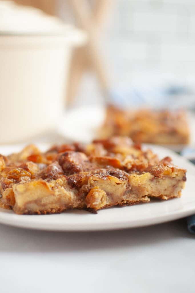 A slice of cinnamon roll casserole on a white plate, showing a soft, custard-like interior with golden raisins and cinnamon-swirl bread pieces.