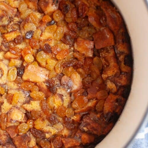 Close-up of a warm, golden-brown cinnamon roll casserole topped with plump golden and dark raisins, baked to perfection in a white dish.