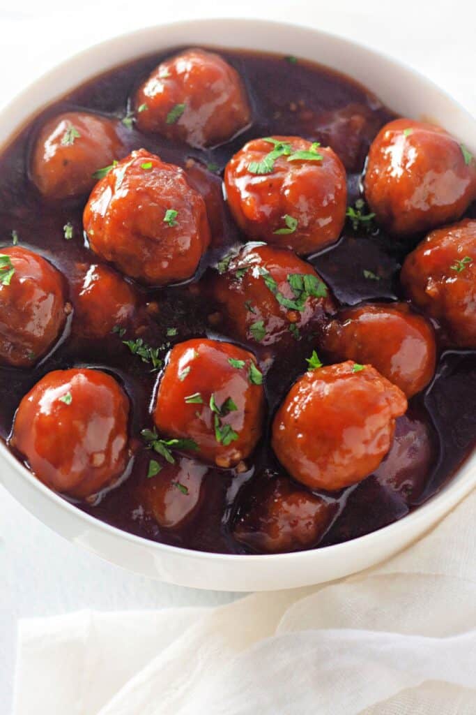 A bowl of honey garlic meatballs coated in a glossy, rich sauce and garnished with finely chopped parsley.