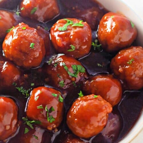 A bowl of honey garlic meatballs coated in a glossy, rich sauce and garnished with fresh parsley.