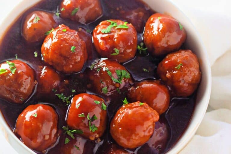 A bowl of honey garlic meatballs coated in a glossy, rich sauce and garnished with fresh parsley.