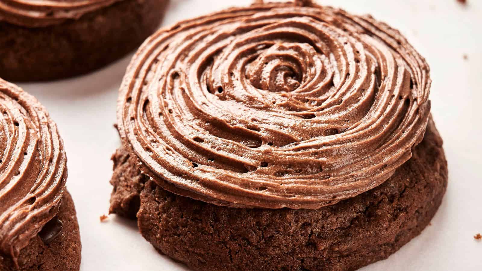 A delectable close-up of a Copycat Crumbl Chocolate Cake Cookie, crowned with a swirl of rich chocolate frosting, resting on a pristine white surface.