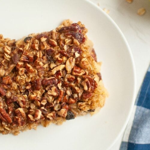 A close-up of a square piece of baked oatmeal with a crunchy pecan topping on a white plate.