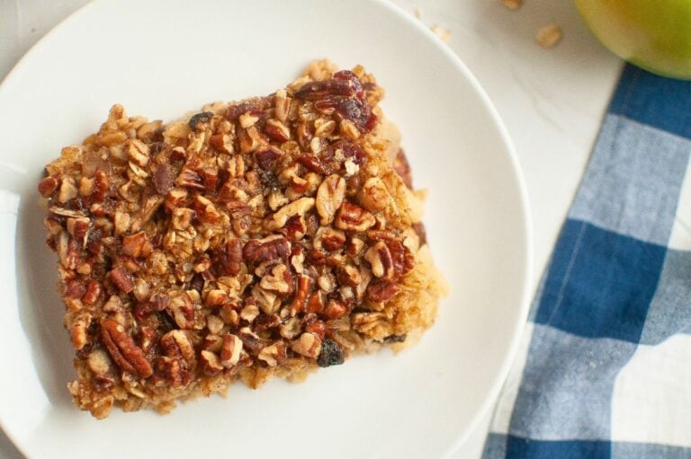 A close-up of a square piece of baked oatmeal with a crunchy pecan topping on a white plate.