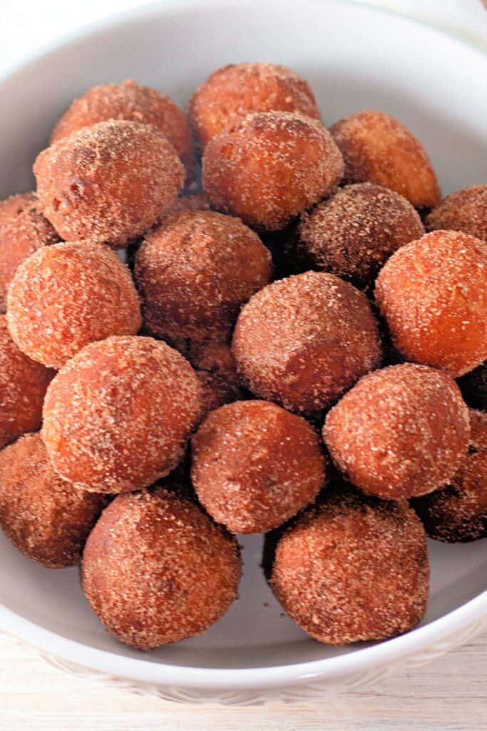 A bowl filled with golden-brown biscuit dough donut holes coated in cinnamon sugar, arranged closely together.