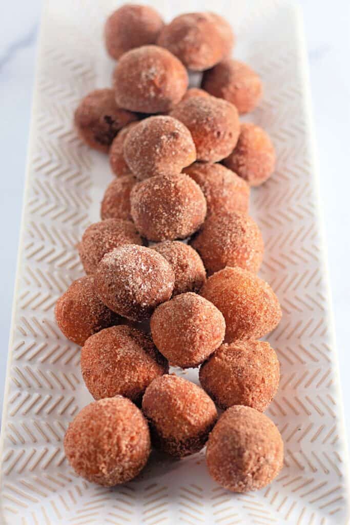 A close-up image of a plate filled with golden-brown biscuit dough donut holes coated in cinnamon sugar.
