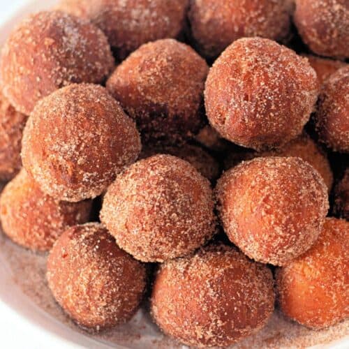 A white bowl filled with golden-brown biscuit dough donut holes, coated in a cinnamon-sugar mixture.