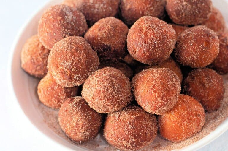 A white bowl filled with golden-brown biscuit dough donut holes, coated in a cinnamon-sugar mixture.