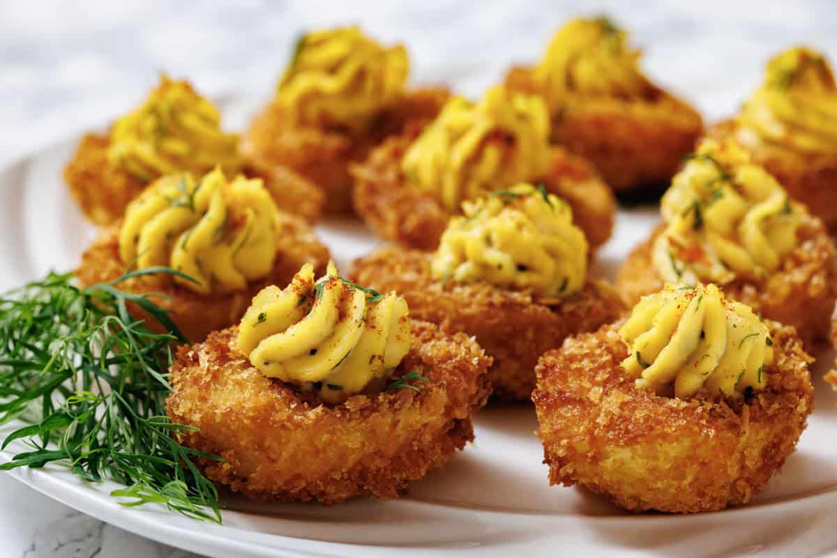 A close-up shot of fried deviled eggs on a white plate, with a focus on the texture and garnish.