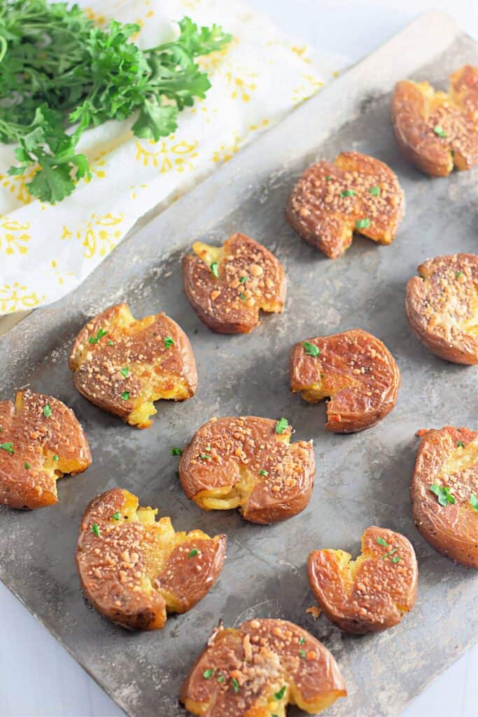 Crispy smashed potatoes with a golden, crunchy crust, sprinkled with Parmesan and fresh herbs. The tender insides peek through the cracked edges.