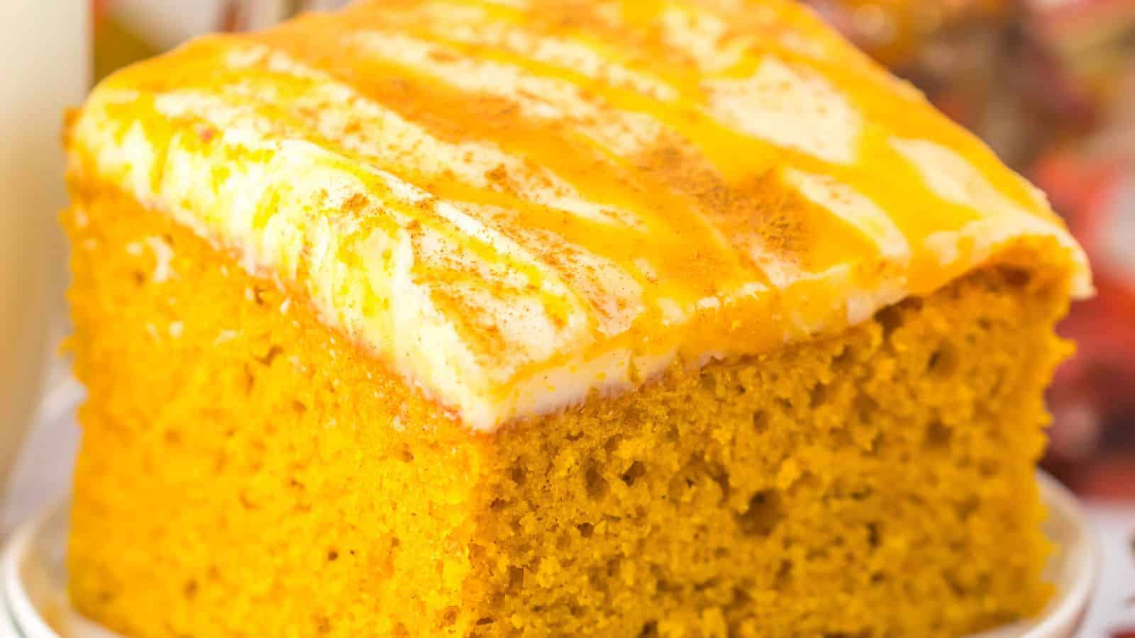 Close-up of a slice of pumpkin cake with cream cheese frosting and a drizzle of caramel on top.