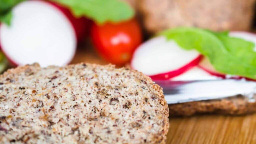 Nutty bun sliced in half with veggies in the background.