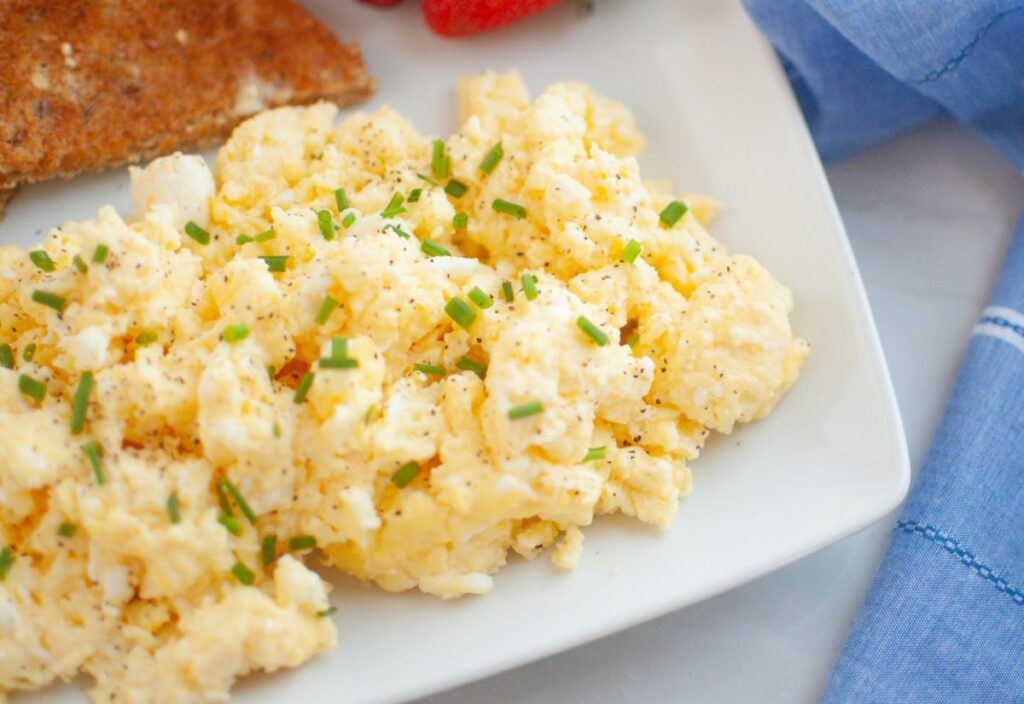 Plate of scrambled eggs with chives, toast, and strawberry.