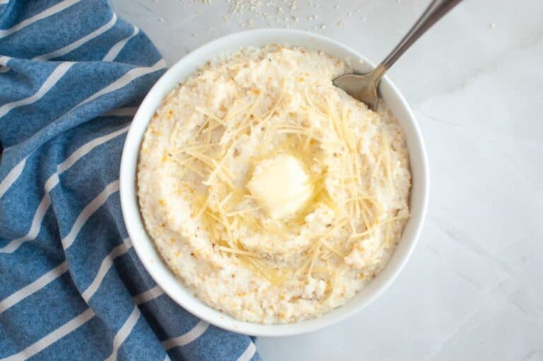 A bowl of creamy Southern-style grits topped with shredded cheese and a melting pat of butter, with a spoon resting inside the bowl.