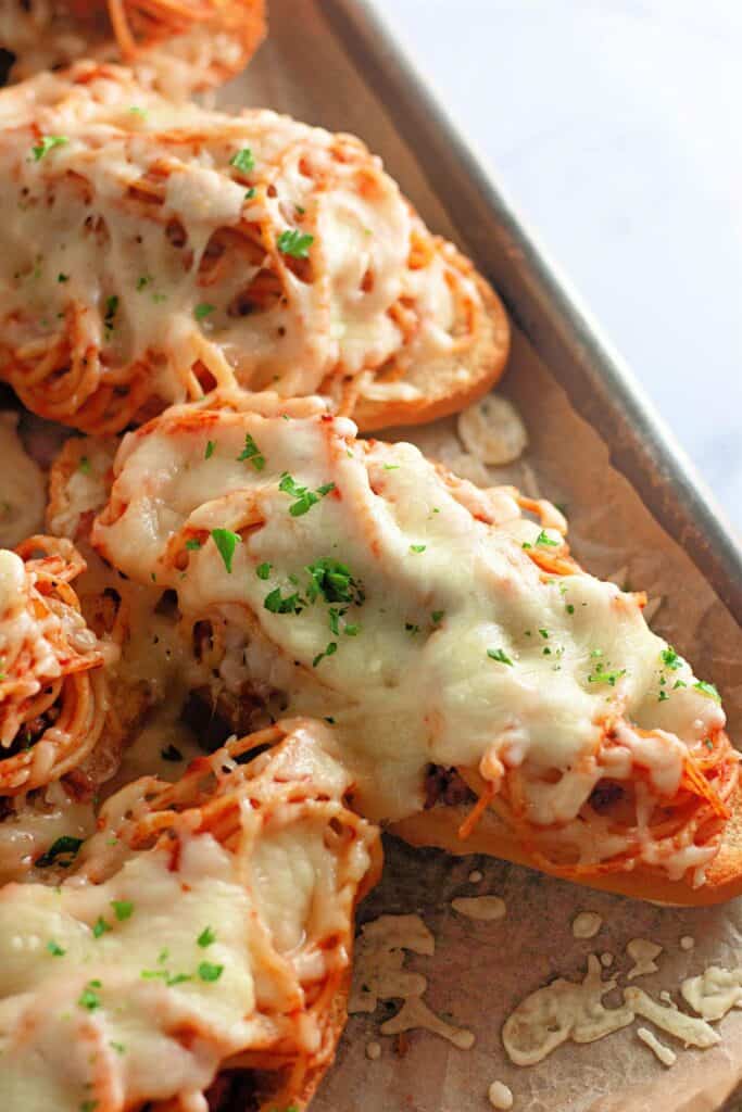 A close-up of cheesy spaghetti bread fresh out of the oven, topped with melted mozzarella and a sprinkle of parsley. The golden, crispy edges and gooey cheese make it a mouthwatering comfort food.