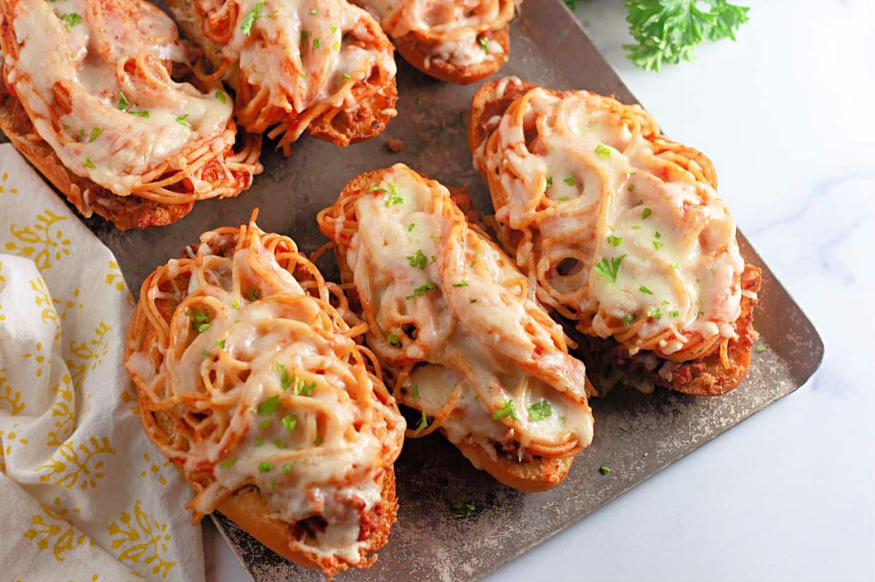 Toasted bread slices topped with spaghetti, marinara sauce, and melted mozzarella cheese, garnished with fresh parsley. A creative and cheesy twist on classic spaghetti, served open-faced and oven-baked.