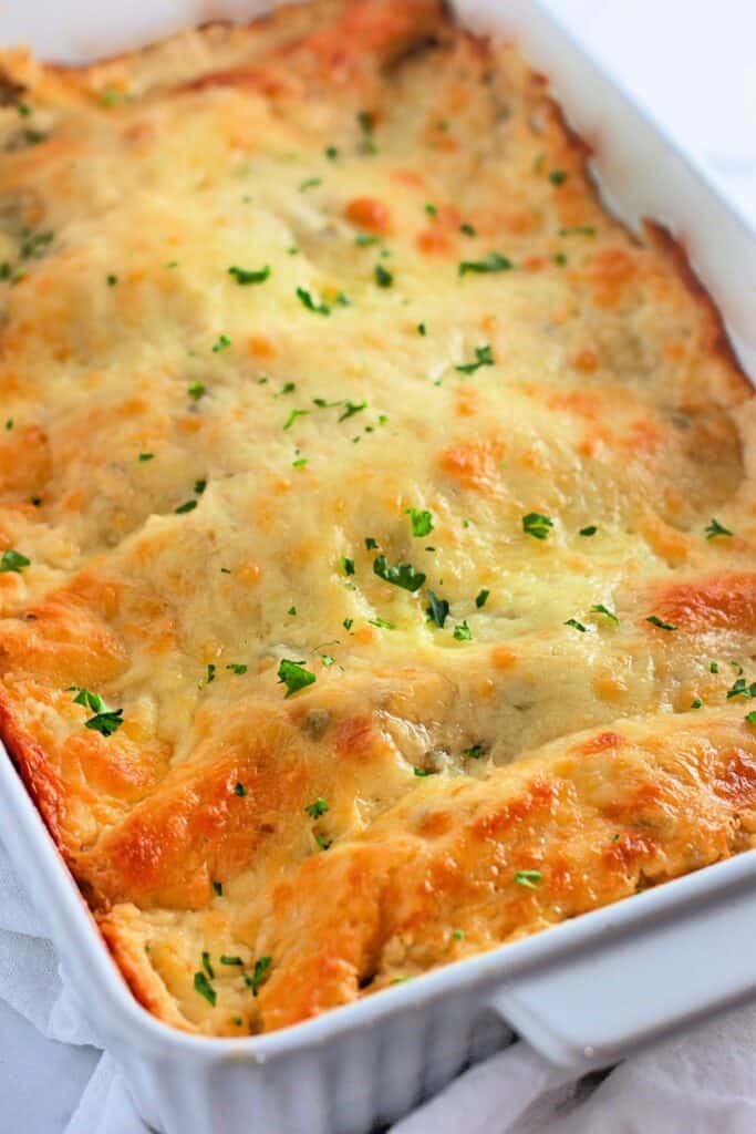 A golden, bubbly layer of melted cheese tops a pan of creamy white chicken enchiladas, with bits of parsley sprinkled on for a fresh touch. The edges are perfectly crisp, giving the dish a warm and comforting look.