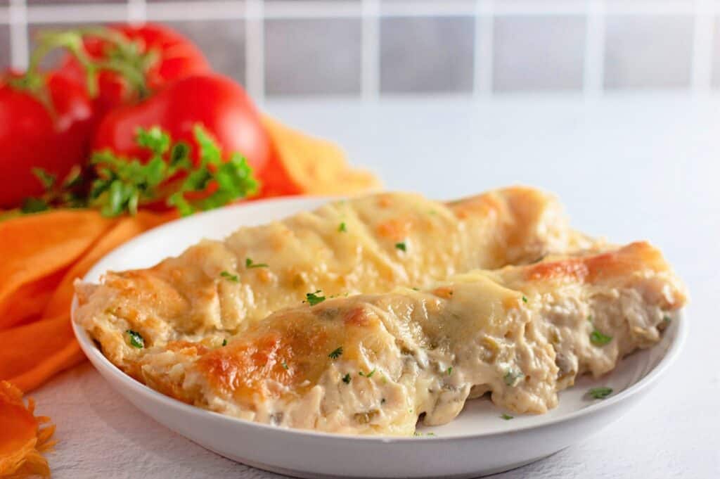 A baking dish filled with creamy white chicken enchiladas, topped with melted cheese and garnished with chopped cilantro. The golden, bubbly sauce covers soft tortillas stuffed with seasoned shredded chicken, creating a comforting and hearty meal.