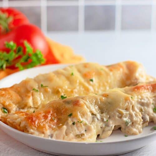 A baking dish filled with creamy white chicken enchiladas, topped with melted cheese and garnished with chopped cilantro. The golden, bubbly sauce covers soft tortillas stuffed with seasoned shredded chicken, creating a comforting and hearty meal.