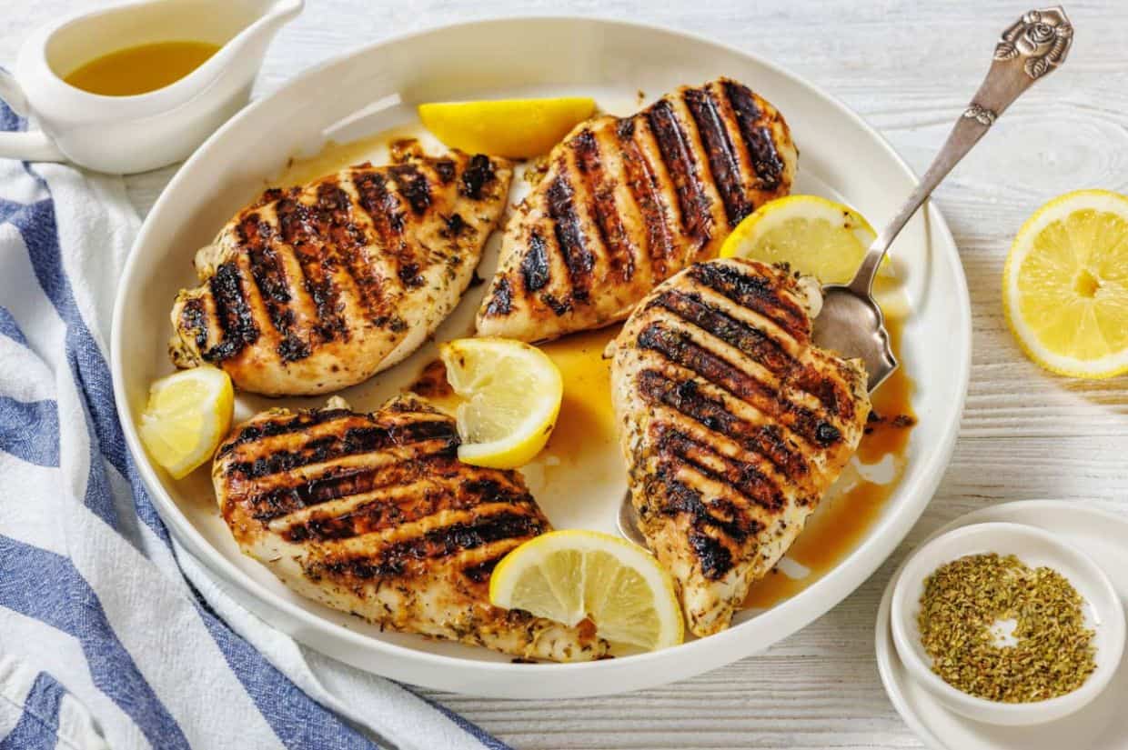 Grilled lemon herb chicken breasts served with lemon wedges on a white plate.