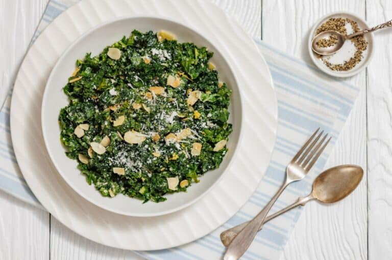 A bowl of fresh kale salad topped with lemon zest, shaved Parmesan cheese, and sliced almonds.