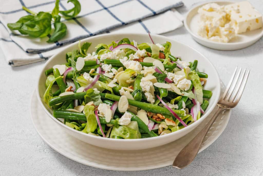 Fresh green bean salad with feta, red onion, and almond slices in a white bowl.