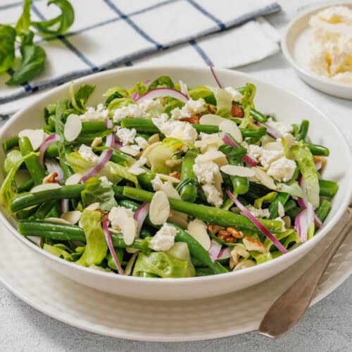 Fresh green bean salad with feta, red onion, and almond slices in a white bowl.