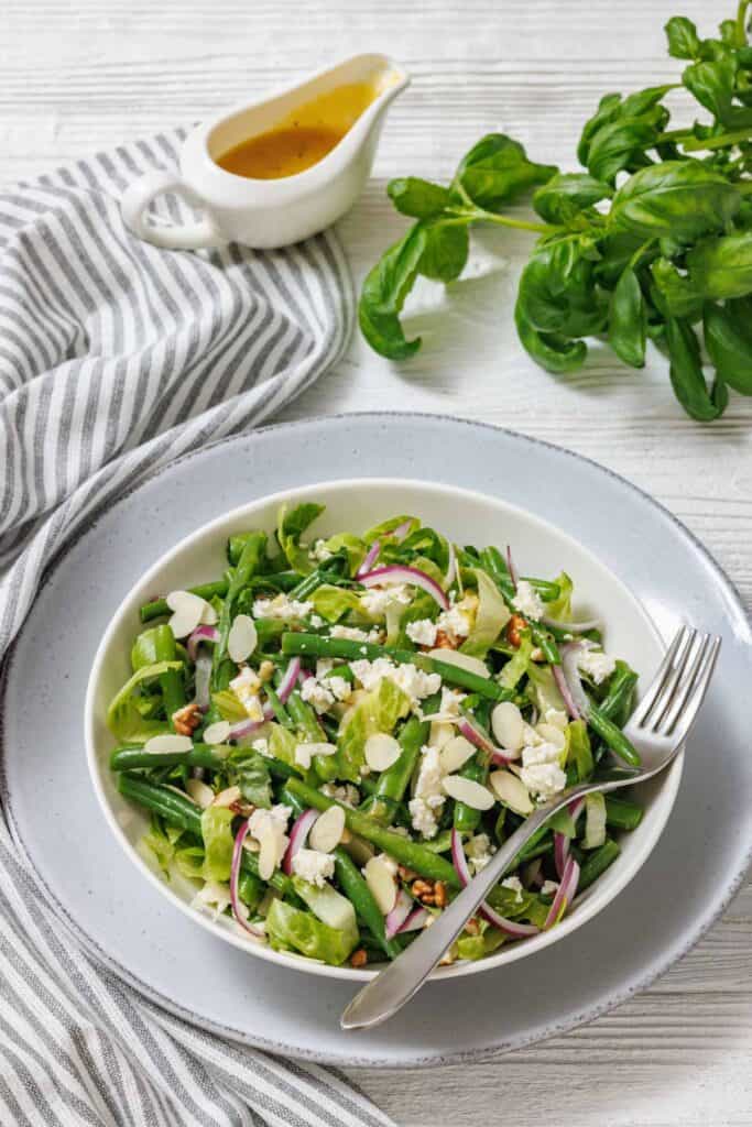 Green bean salad with goat cheese, almonds, and red onion, served with dressing and chopped nuts on the side.