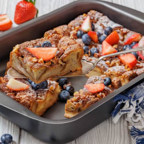 A hand with a spoon hovers over a pan containing a slice of bread being prepared.