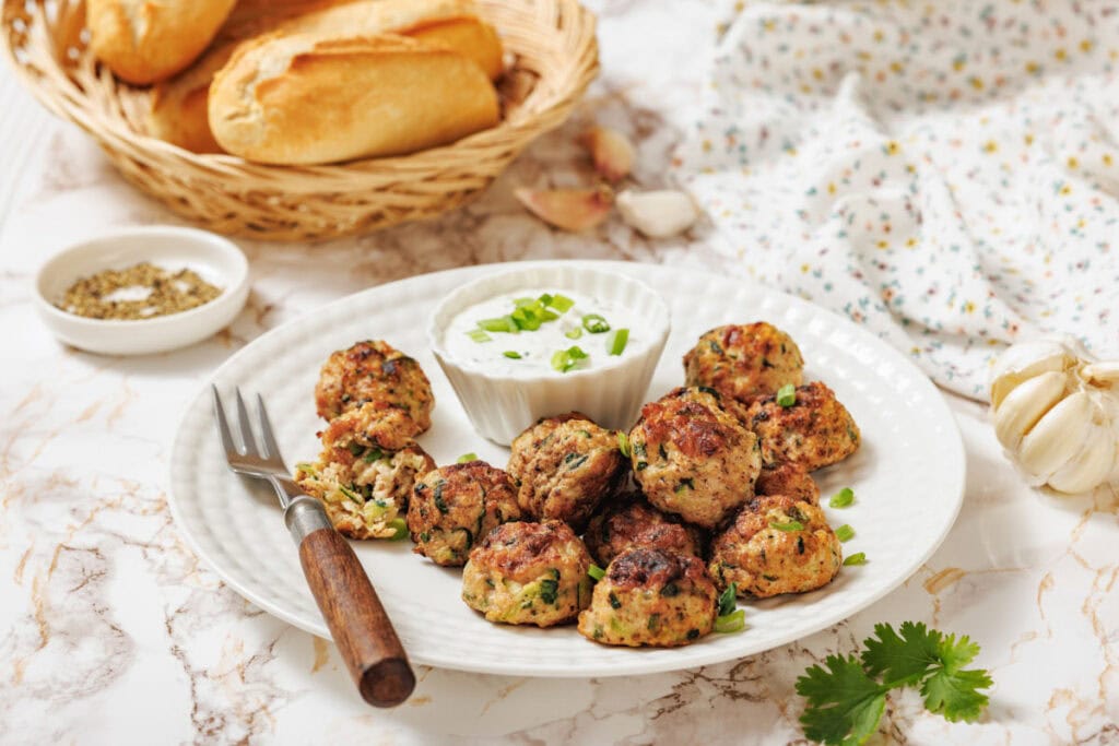 A white bowl filled with golden-brown meatballs garnished with chopped herbs.