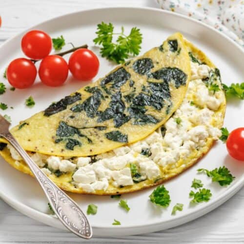 A spinach and feta omelette on a white plate, garnished with parsley and surrounded by cherry tomatoes.
