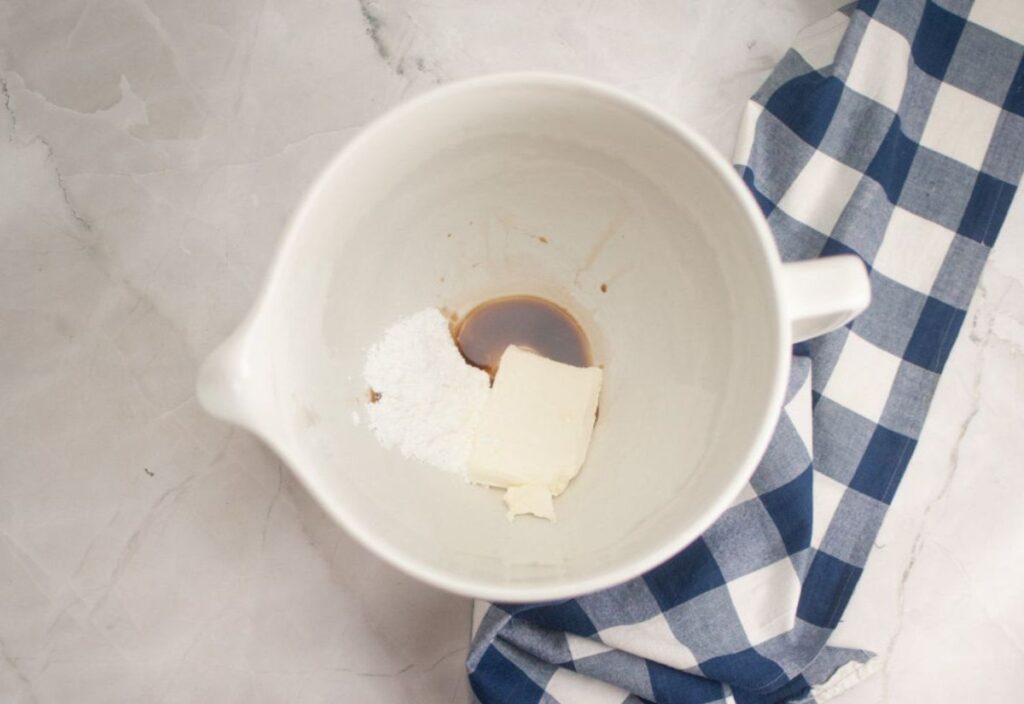 Ingredients for the recipe: cream cheese, powdered sugar, and vanilla extract in a mixing bowl.