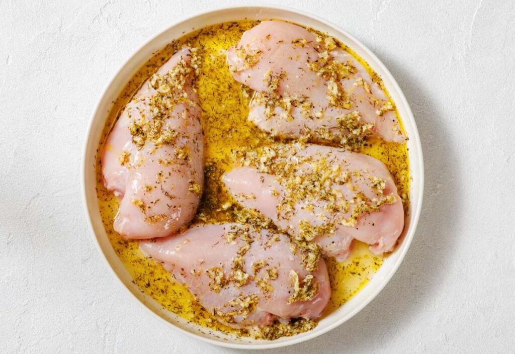 A plate filled with marinated raw chicken breasts.
