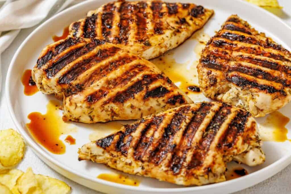 Grilled chicken breasts with charred grill marks, drizzled with sauce on a white plate, exuding a savory aroma.