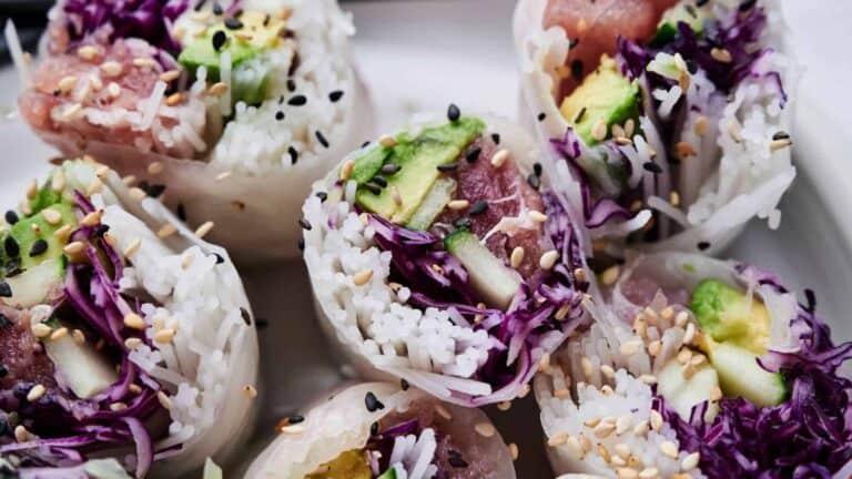 Close-up of sliced spring rolls filled with rice, avocado, purple cabbage, and sesame seeds, arranged on a white plate.