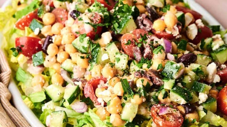 A fresh salad with chopped cucumbers, cherry tomatoes, chickpeas, red onion, feta cheese, black olives, and parsley on a bed of lettuce.