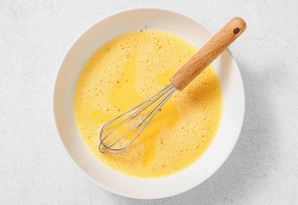 Egg mixture in a large mixing bowl with a whisk.