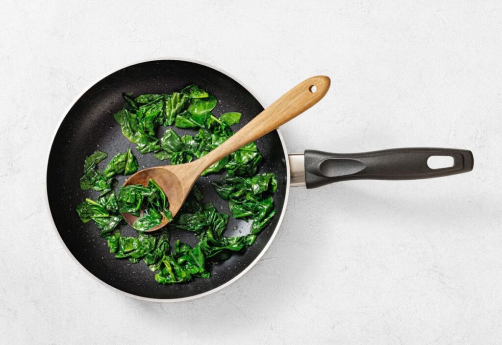 Wilted spinach in a non-stick pan with a wooden spoon.