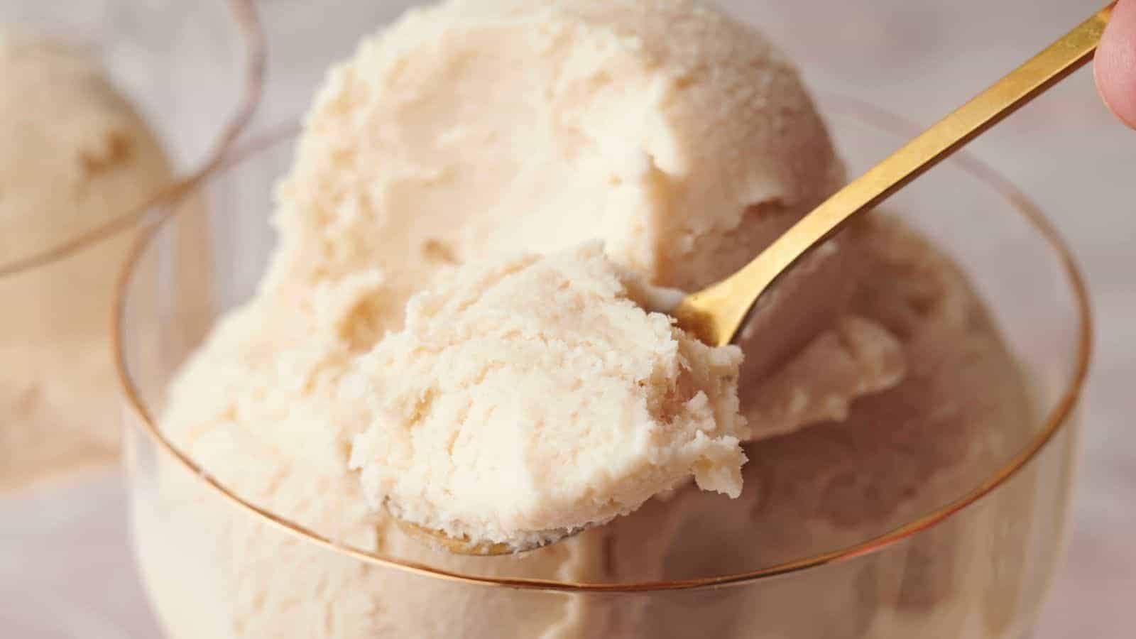 A gold spoon scoops a portion of creamy, pale vanilla ice cream from a glass bowl.