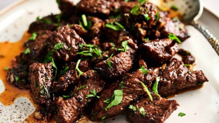 Close-up of cooked beef chunks garnished with chopped herbs on a plate with a spoon nearby.